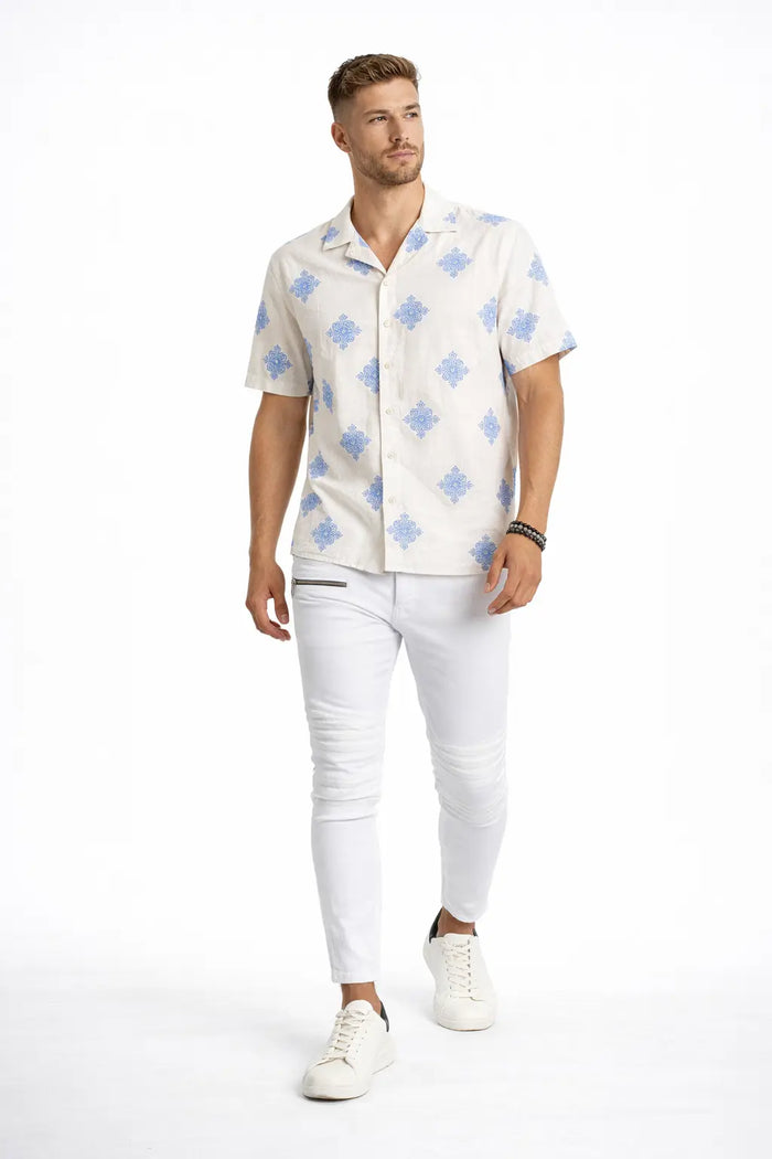A man walks confidently in a short-sleeve patterned shirt and slim white jeans, paired with casual sneakers.