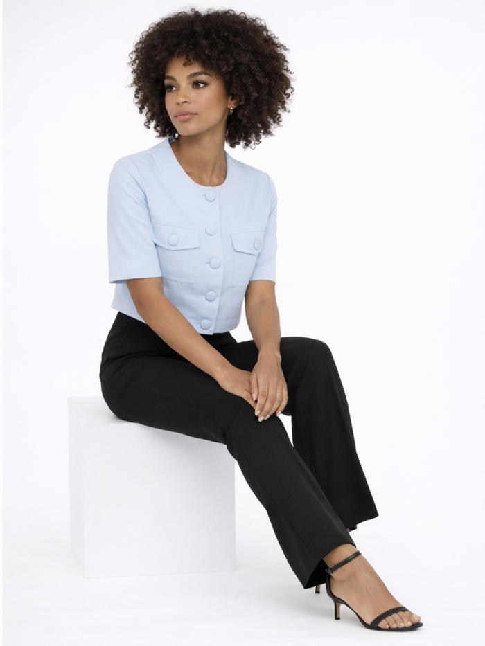 A model with curly hair wears a light blue cropped top with buttons, paired with black pants and strappy heels.
