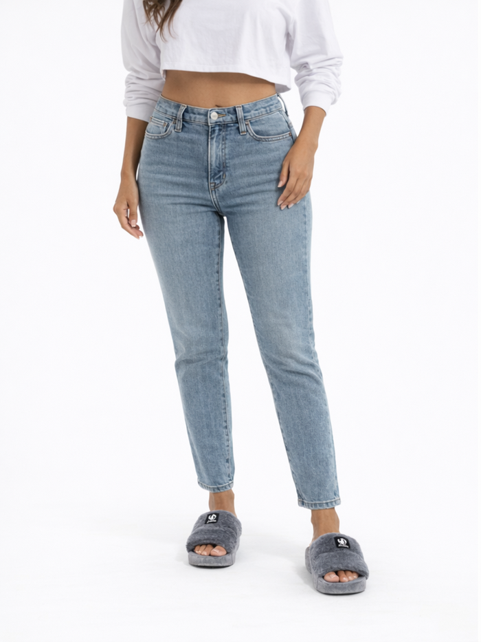 A person wearing light blue high-waisted jeans and gray fuzzy slides, standing against a plain white background.