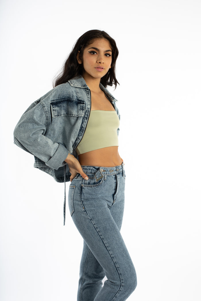 Aubri oversized blue wash denim jacket styled over a sage green tube top and matching jeans for a streetwear vibe.