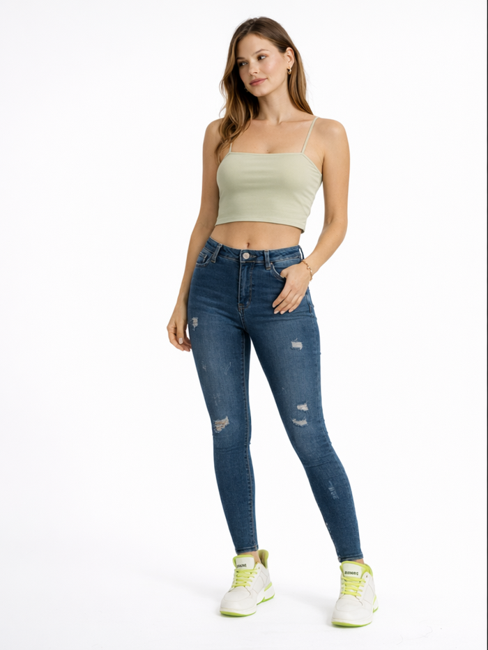 A woman stands confidently in a light green cropped top, distressed blue jeans, and white sneakers with green accents.