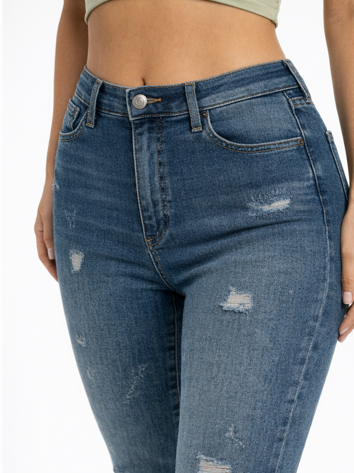 Close-up of a person wearing distressed blue denim jeans with a high waist and a button closure.