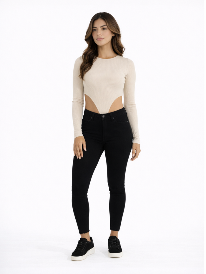A model poses in a fitted beige long-sleeve top with cut-out details, paired with black skinny jeans and sneakers.