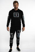 Model in black distressed joggers with blind frame graphic patches, styled with a matching hoodie and black sneakers.