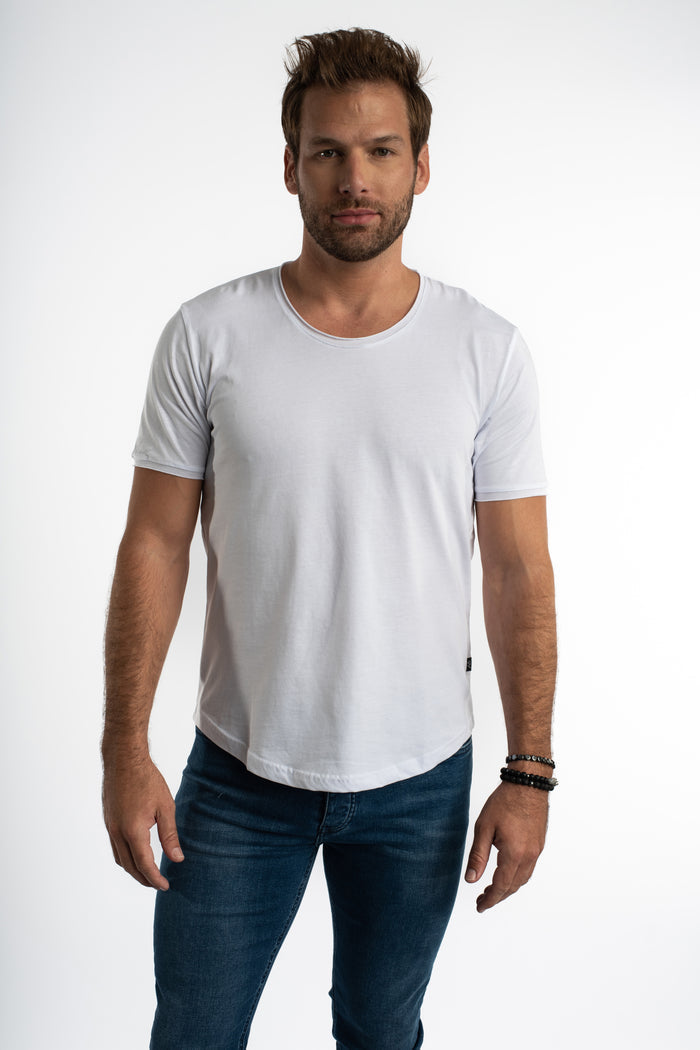 Model wearing a Carbon white streetwear tee with a scoop neck and curved hem, paired with blue denim jeans.