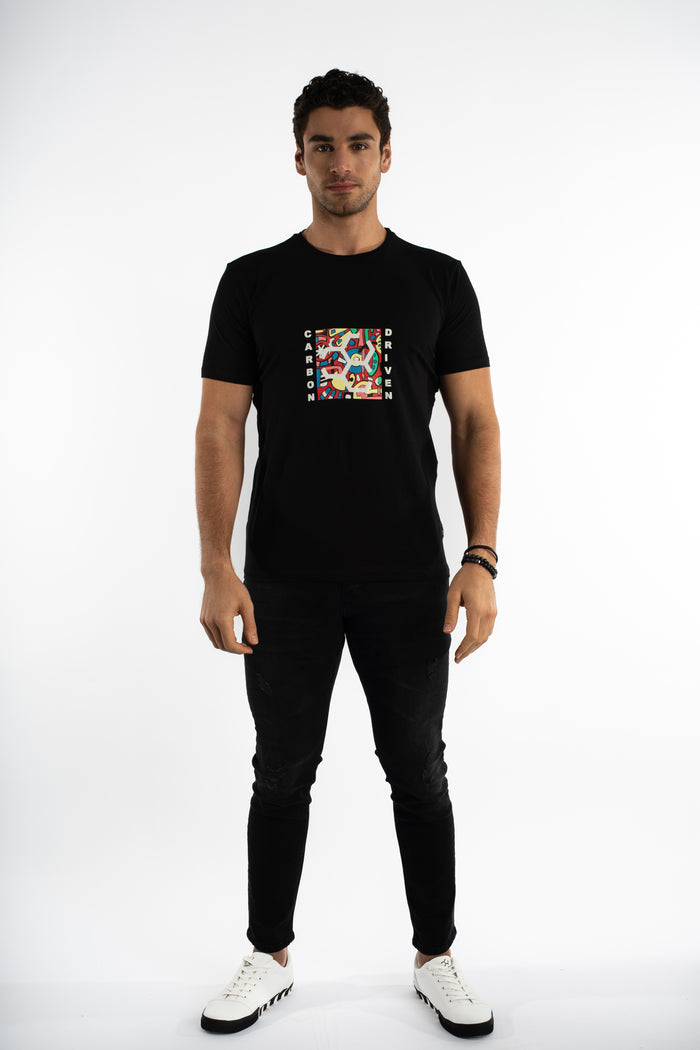 Man wearing a black Driven Graphic Tee with a colorful Carbon chest print, black skinny jeans, and white sneakers.
