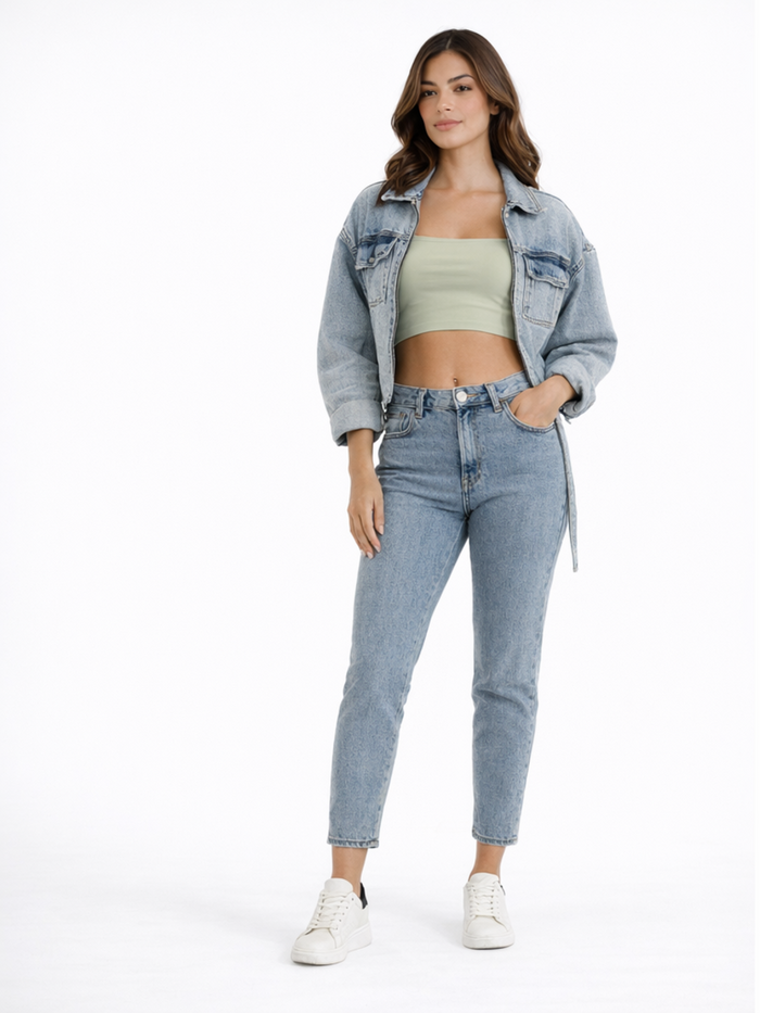 A woman stands confidently in a cropped denim jacket, fitted green top, and light blue jeans, paired with white sneak...