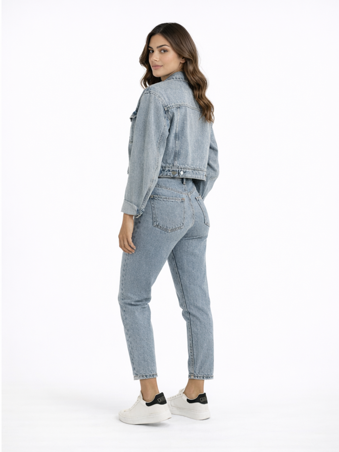 A woman with long hair poses in a light blue denim jacket and matching jeans, showcasing a casual outfit.