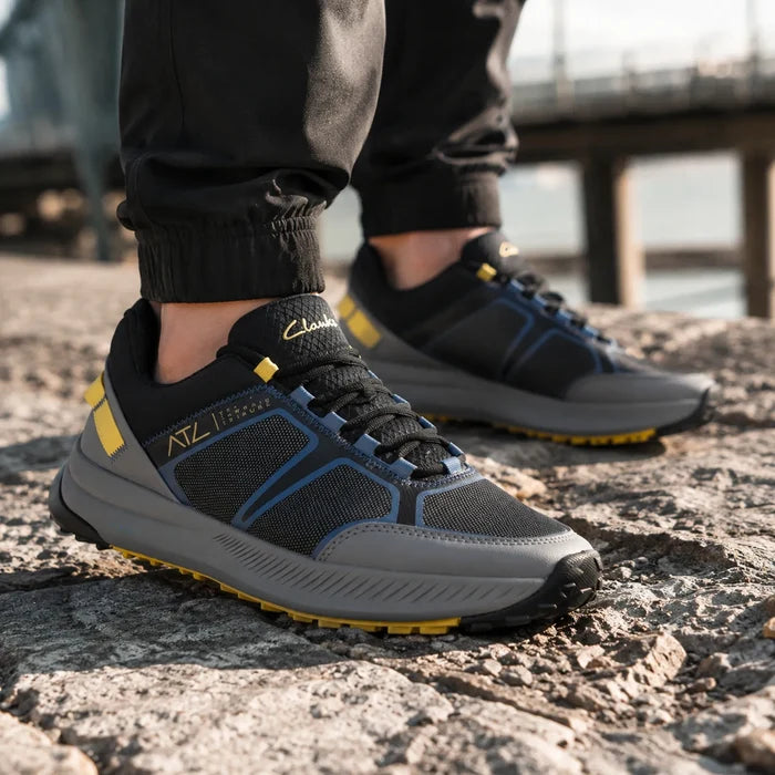 Black trail sneaker with blue upper panels, gray sole, and yellow tread accents