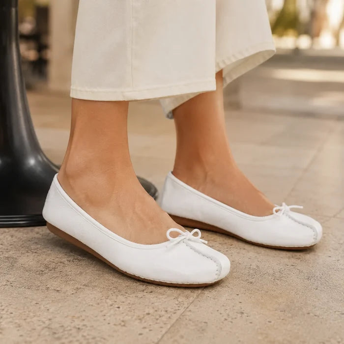 Close-up of women’s white leather ballet flats with bow tie and brown textured sole.