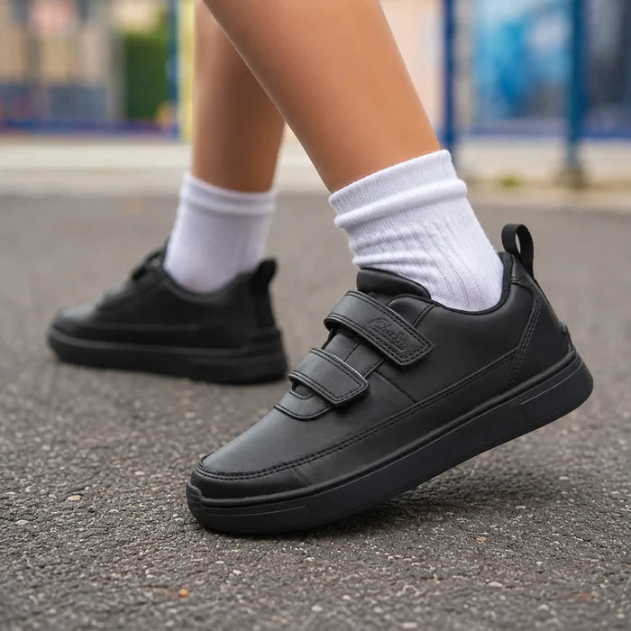 Black kids sneakers with dual hook-and-loop straps on pavement with white socks