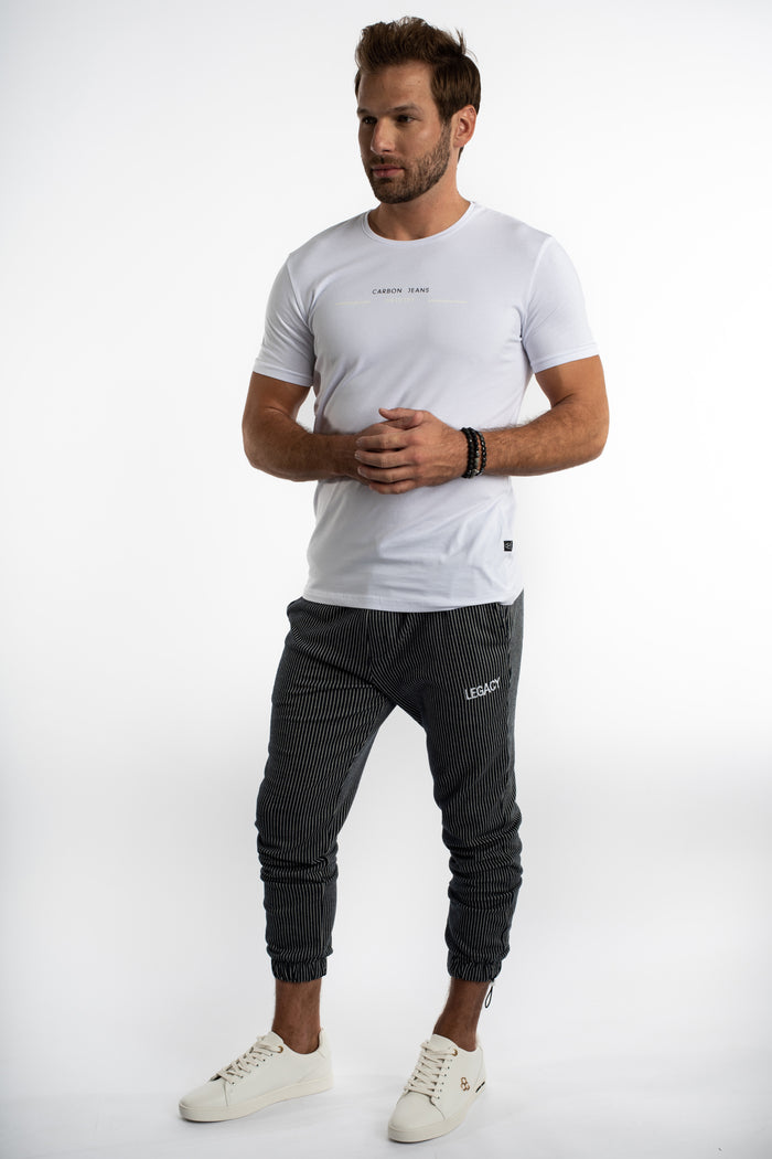 Man in a white Carbon Jeans Classic Industry streetwear t-shirt with pinstripe joggers and white sneakers.