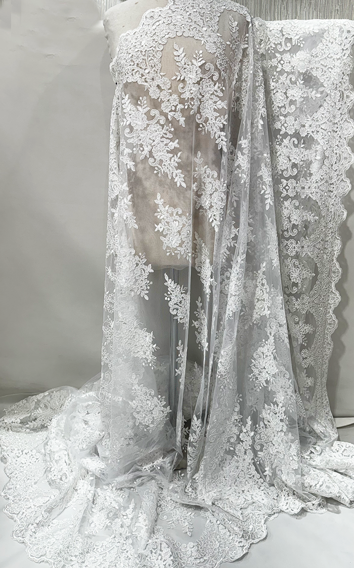 A piece of white corded lace fabric with floral patterns displayed against a neutral background.