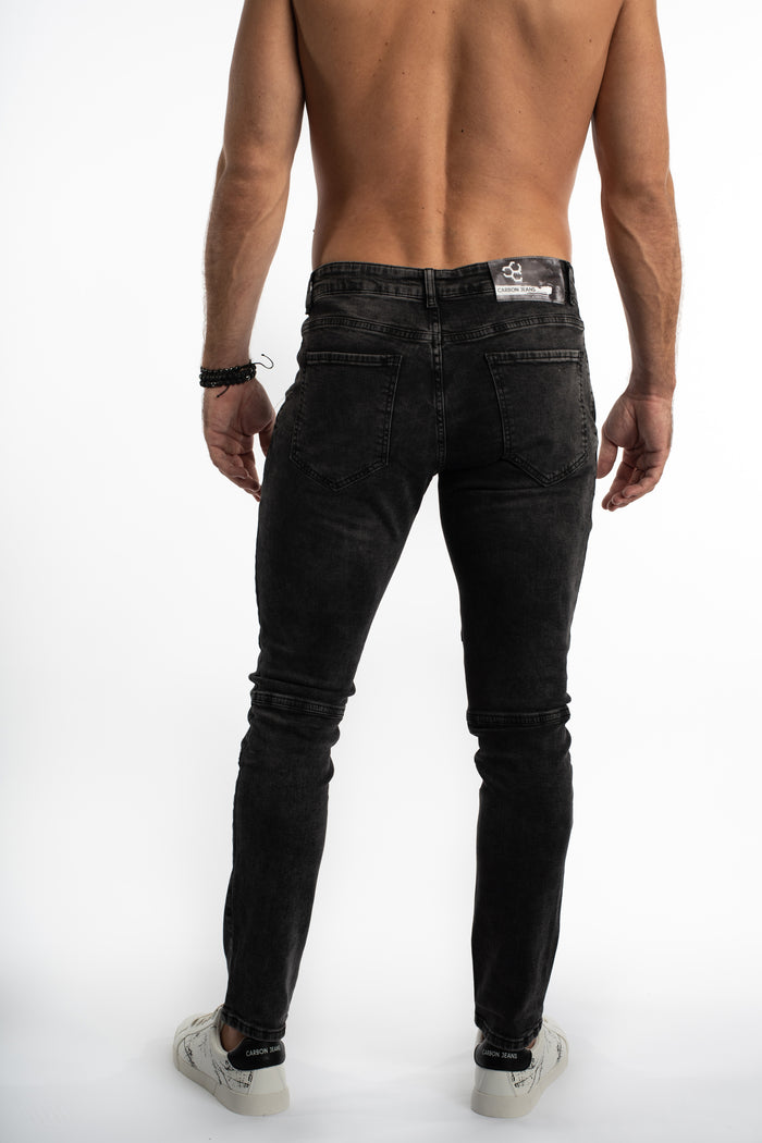 A man stands with his back to the camera, wearing fitted black jeans and white sneakers.