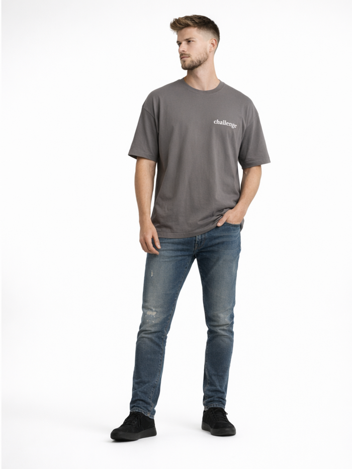 A man stands confidently in a gray t-shirt and distressed blue jeans, paired with black sneakers.