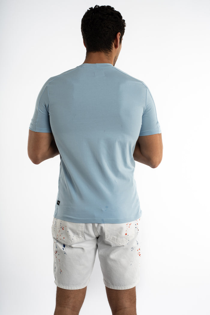 Back view of a man wearing the light blue Element Essential Streetwear Tee with white paint-splatter denim shorts.