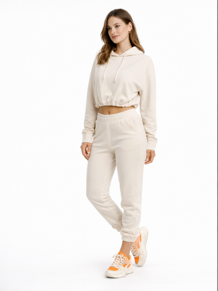 A model poses in a light beige cropped hoodie and matching joggers, paired with sporty sneakers.