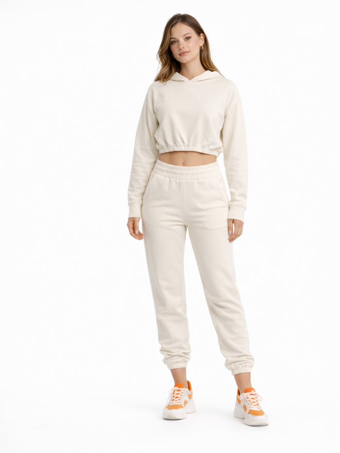A model wearing a light beige cropped hoodie and matching joggers, paired with sporty sneakers.