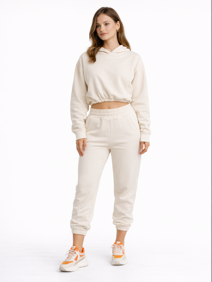 A model wearing a cream-colored cropped hoodie and matching joggers, paired with sporty sneakers.