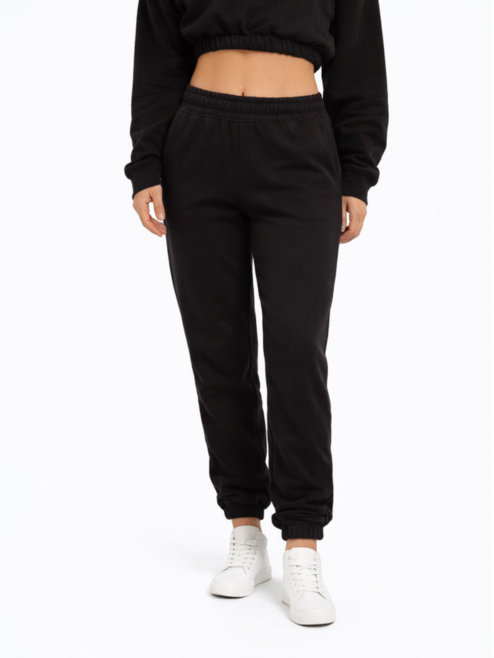 A person wearing black jogger pants with an elastic waistband and white sneakers, standing against a plain background.