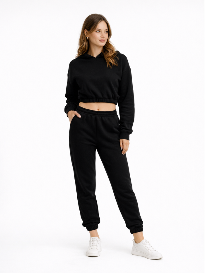 A woman models a black cropped hoodie and matching joggers, paired with white sneakers, against a plain background.