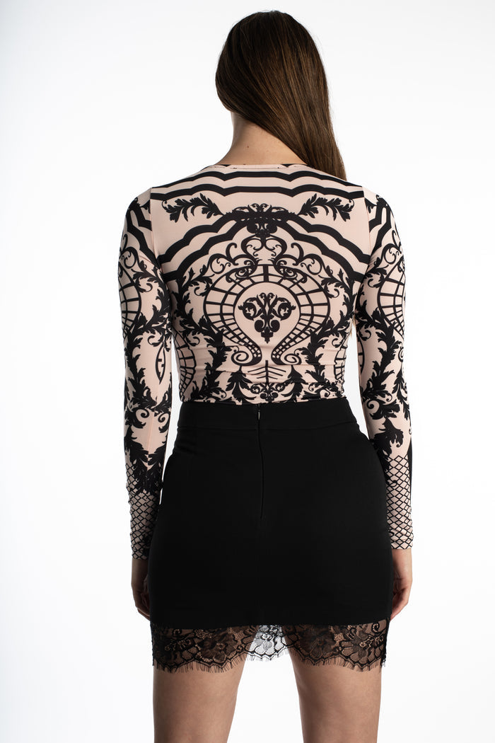 Back view of Elora long-sleeve nude bodysuit with black baroque print, paired with a black lace-trim mini skirt.