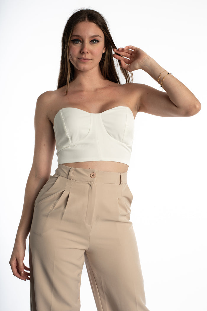 Model wearing the white Emmie Strapless Bustier, a structured corset-style crop top paired with beige trousers.