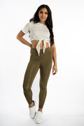 Model in olive green Emory high-waisted leggings by Carbon with a sculpting fit and a white tie-front crop top.