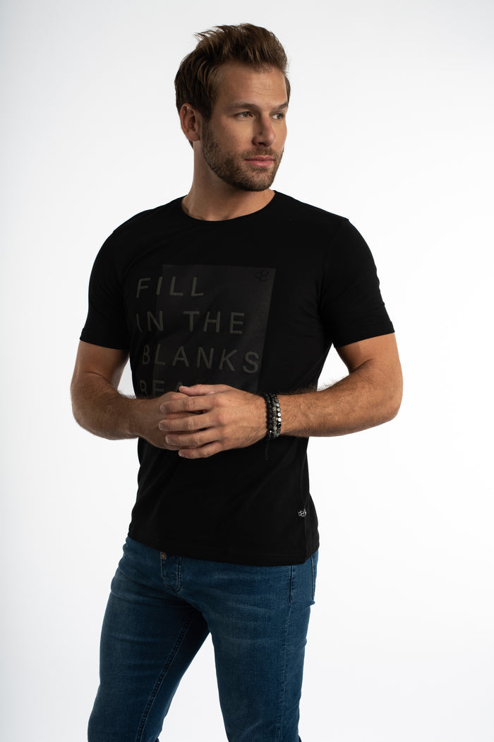 Model wearing Carbon black streetwear graphic tee with tonal embossed FILL IN THE BLANKS lettering and blue jeans.