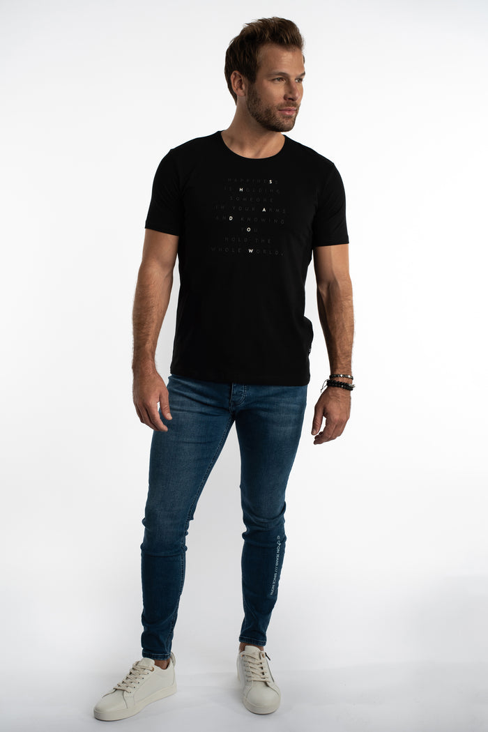 Man in Finn Slim Fit Blue Denim Jeans and black graphic t-shirt for a streetwear look against a white background.