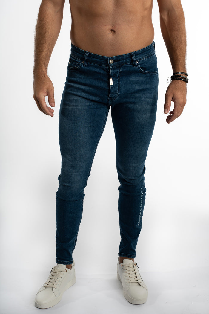 Finn Slim Fit Blue Denim Jeans by Carbon with light wash, side leg branding, and white sneakers streetwear style.