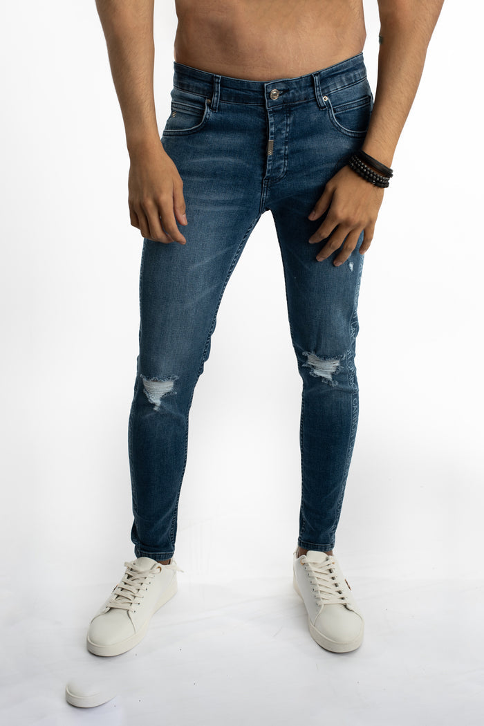 Men's Finnley blue slim fit distressed jeans with knee rips and Carbon side logo detail, paired with white sneakers.