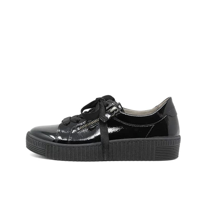 Black glossy sneakers with lace-up and front zipper on a ribbed sole.
