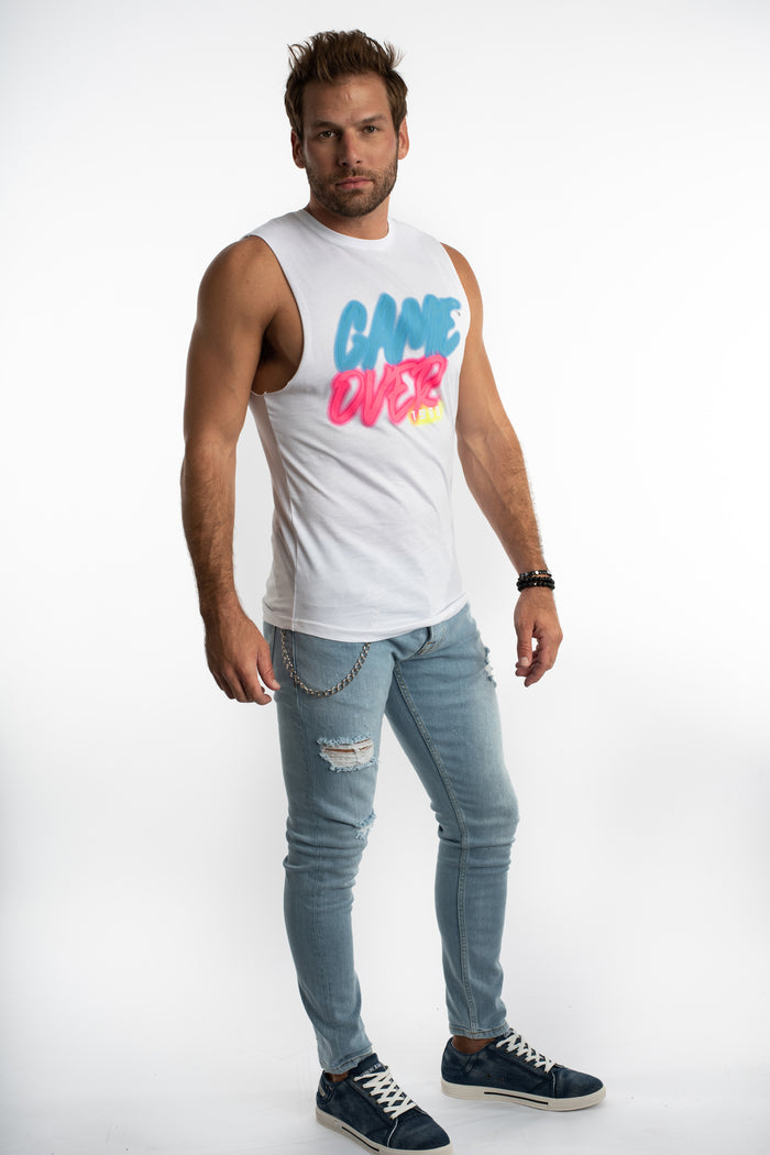 Men's white Game Over streetwear tank top with pink and blue graffiti graphic, paired with light wash distressed jeans.