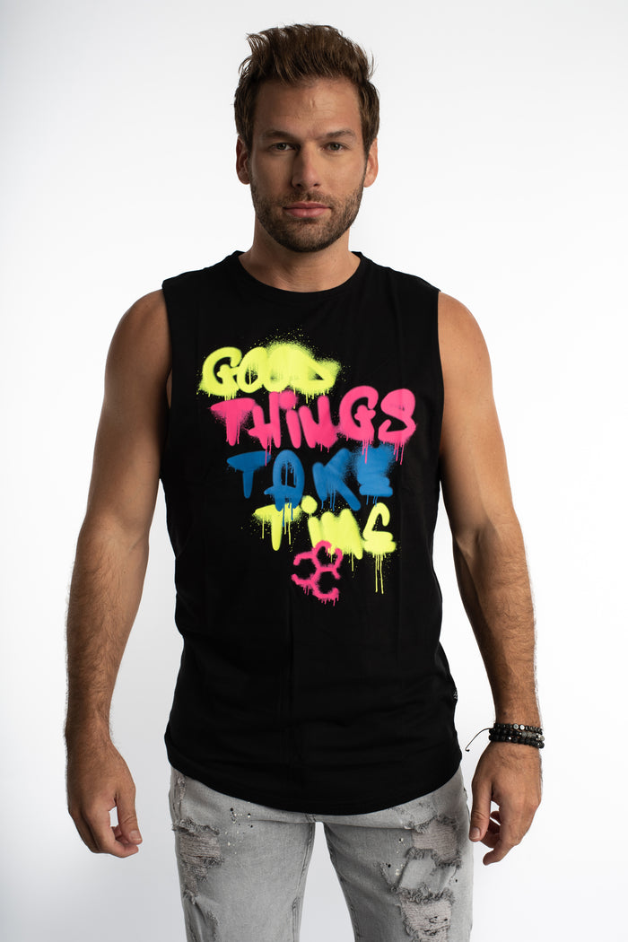 Men's black streetwear tank top with neon 'Good Things Take Time' graffiti graphic worn with light wash jeans.