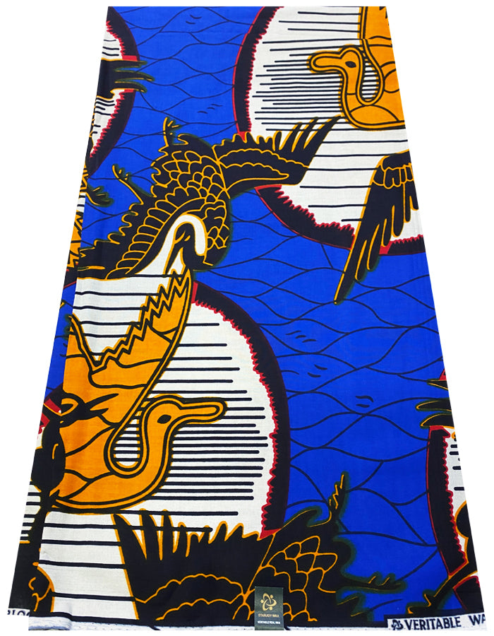A piece of African wax print fabric featuring vibrant patterns in royal blue, orange, dark blue, white, red, and black colors, with a bird and geometric design.