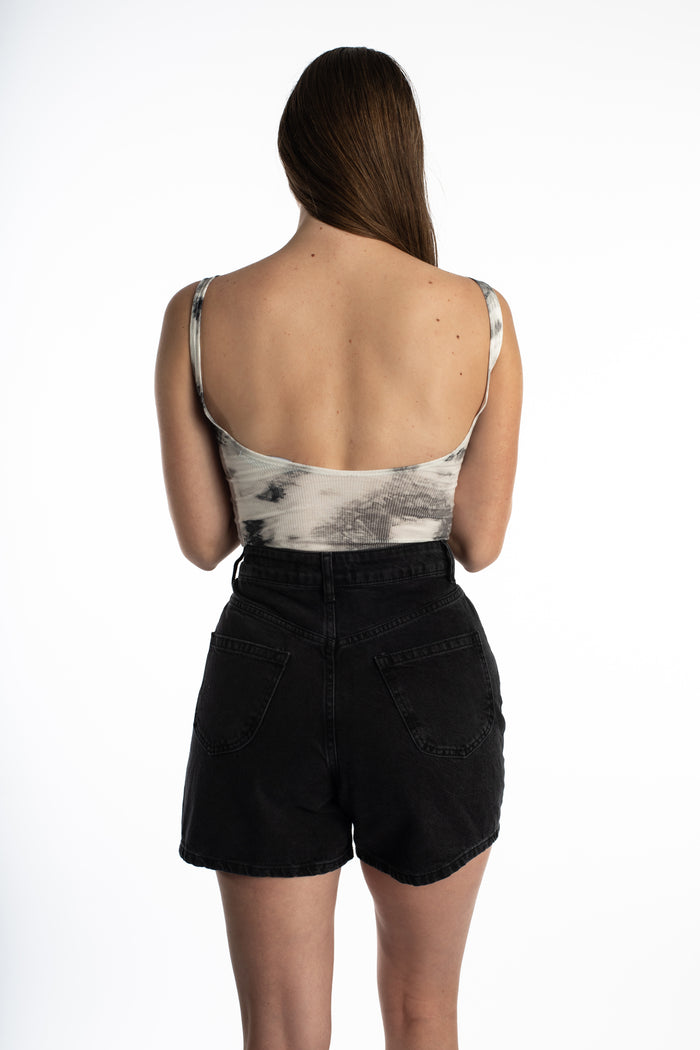 Back view of woman in Harmoni grey tie-dye seamless bodysuit and black denim shorts, highlighting the chic scoop back.