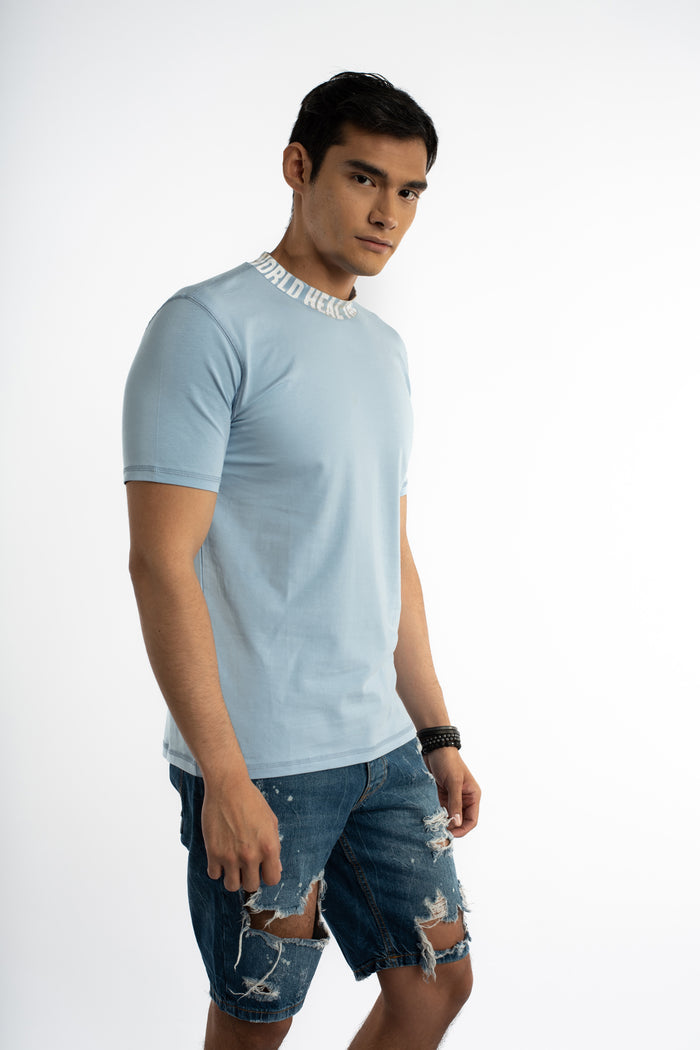Man in light blue Heal the World graphic tee with white text on the collar and distressed denim streetwear shorts.