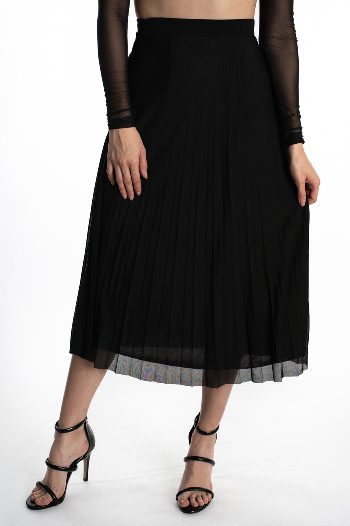 Model in a high-waisted black pleated midi skirt with a sheer hem, styled for a night out with strappy heels.