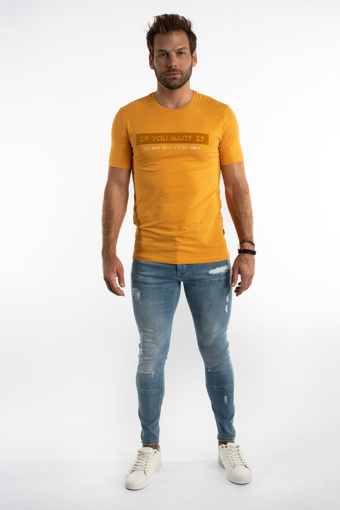 Model wearing Jairo Blue Washed Jeans with biker-style stitching, distressing, and a mustard yellow streetwear t-shirt.