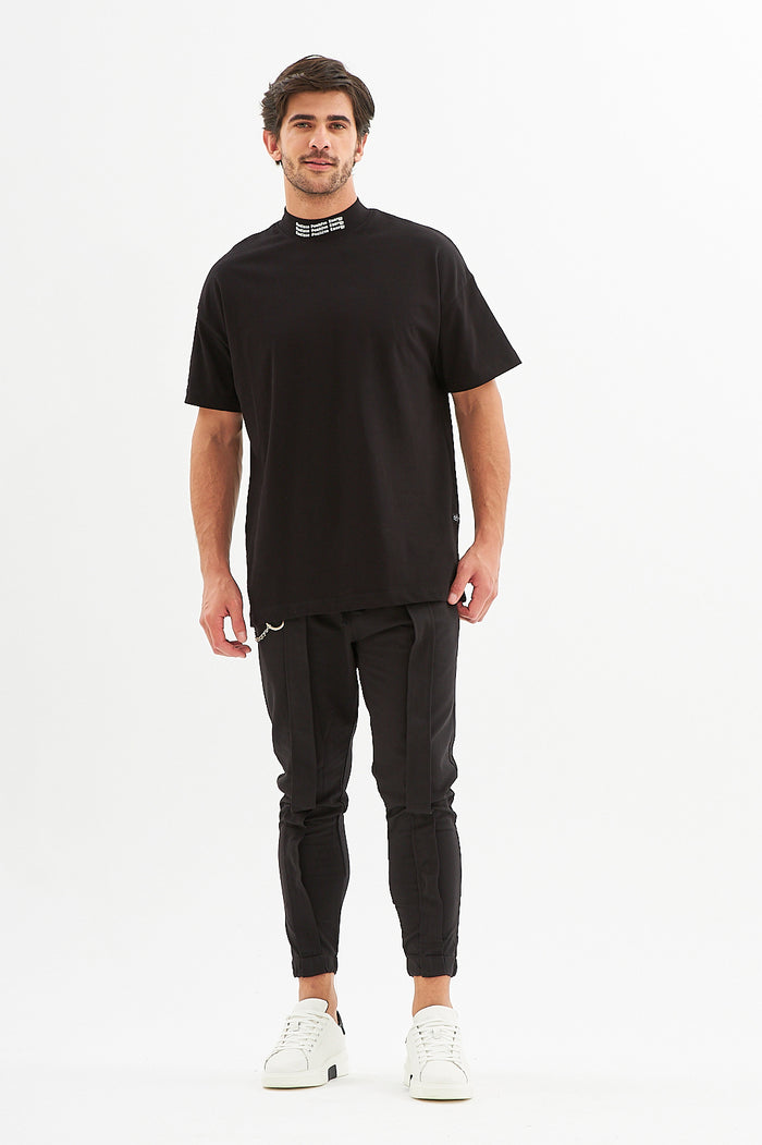 Man in James Black Denim Streetwear Pants with straps and a black mock neck tee against a white background.