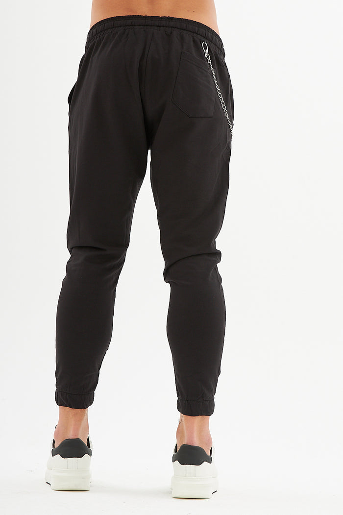 Rear view of black denim streetwear pants with elastic jogger cuffs, silver chain detail, and trendy urban fit.