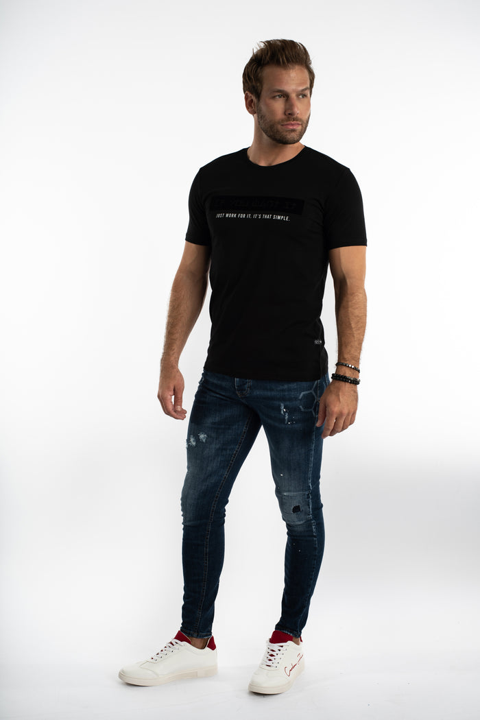 Model in Carbon Jeans Jaxx slim fit blue washed denim with distressed detailing, styled with a black tee and sneakers.