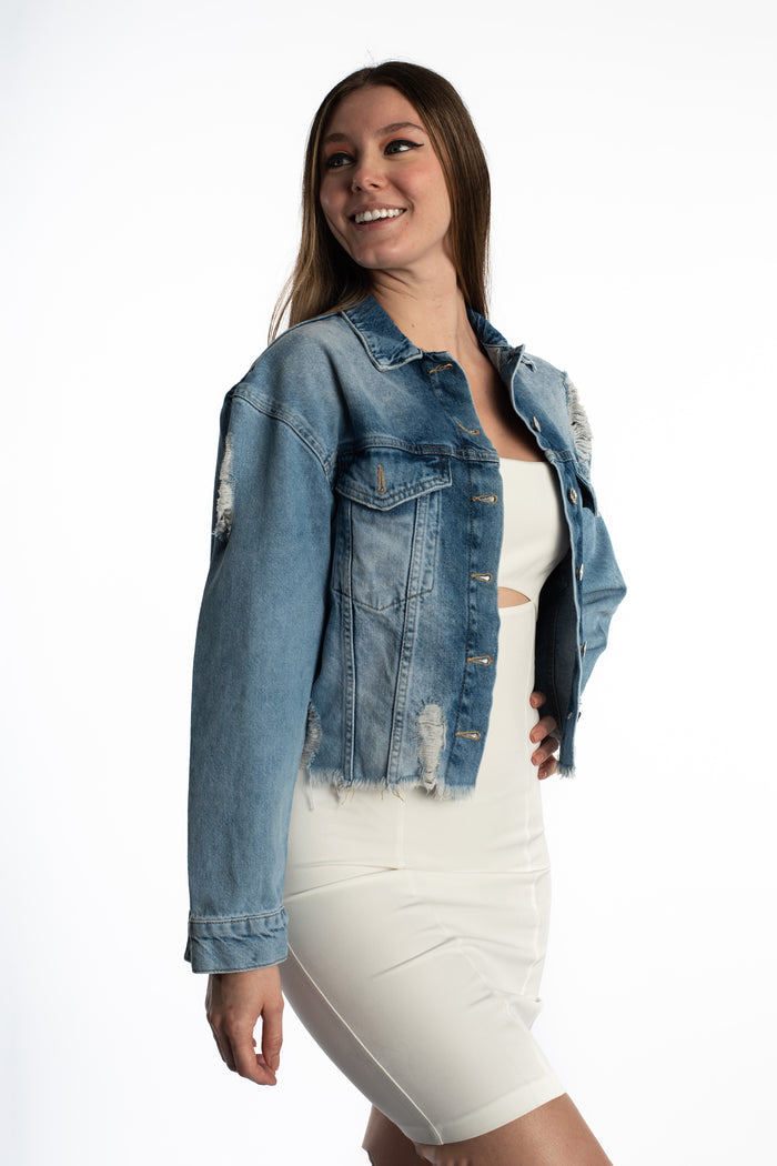 Jolie oversized blue washed denim jacket with distressed frayed hems worn over a white dress for a streetwear aesthetic.
