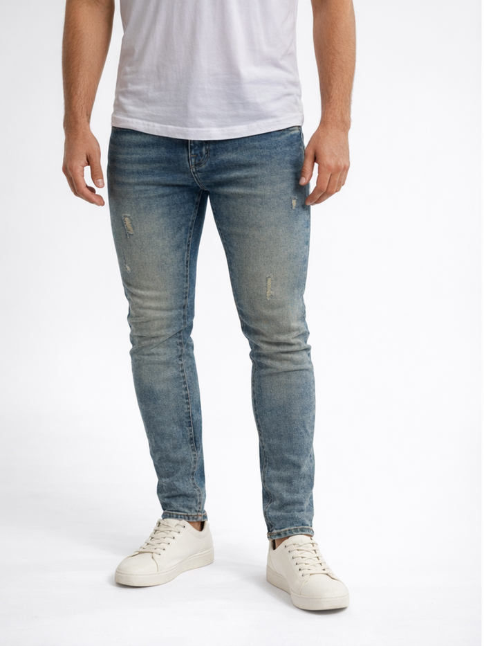 A man wearing light blue distressed jeans and white sneakers, standing against a plain background.