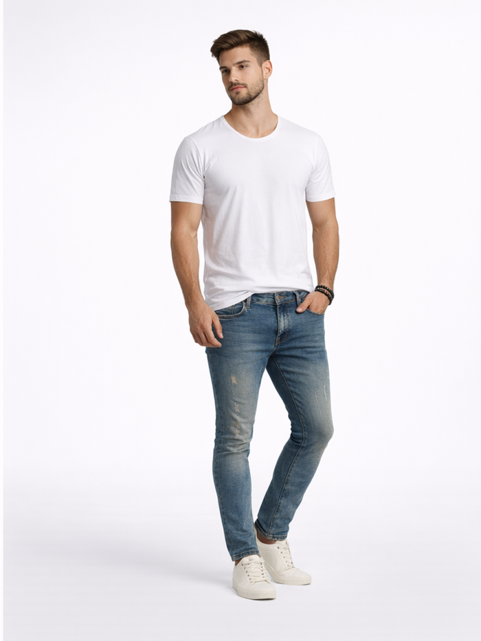 A man stands confidently in a fitted white t-shirt and distressed blue jeans, paired with white sneakers.