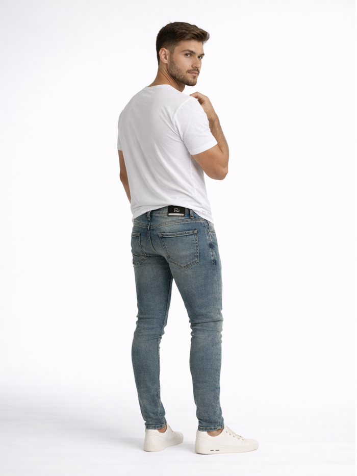 A man in a fitted white t-shirt and blue jeans stands with his back to the camera, showcasing casual footwear.