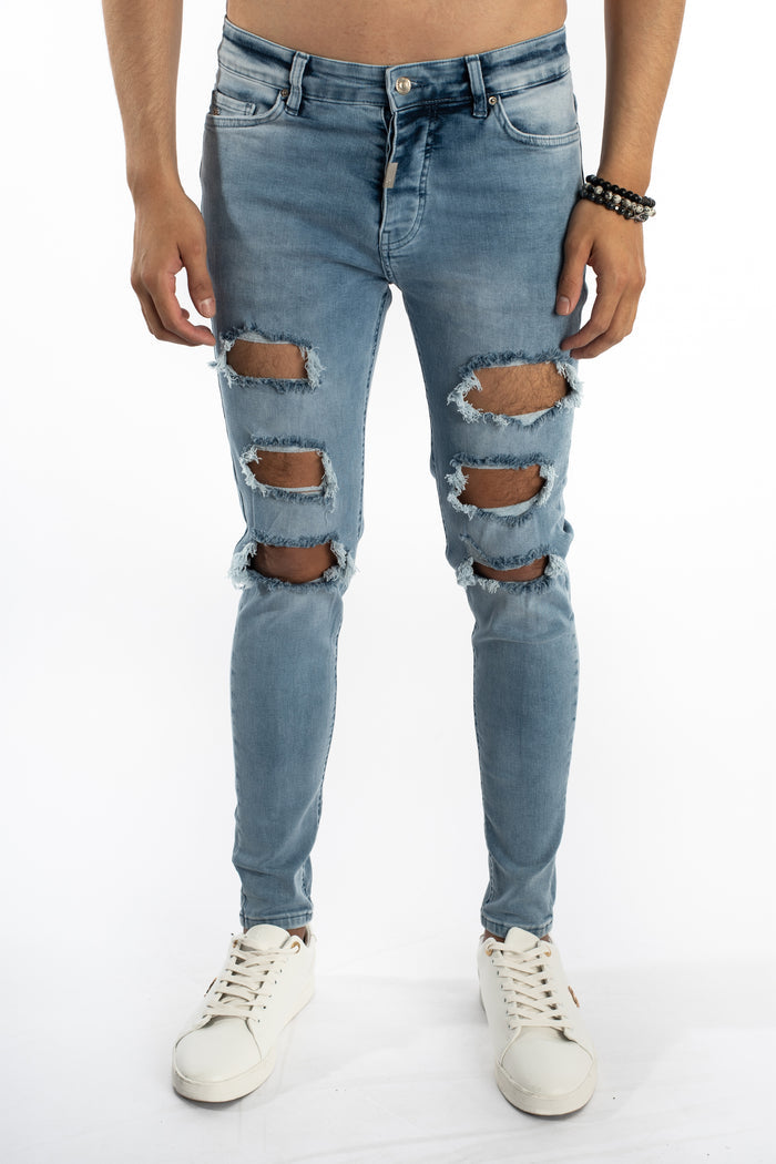 Men's Carbon Kase jeans in light blue washed denim with heavy knee distressing and slim fit, styled with white sneakers.