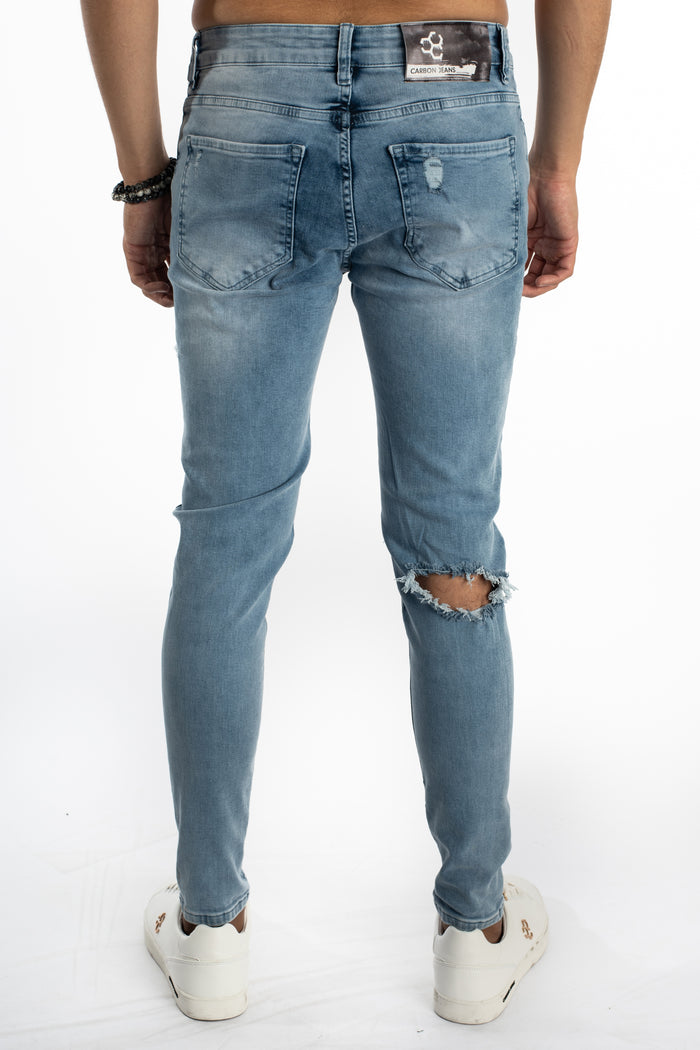 Rear view of Kase blue washed skinny jeans for men, featuring distressed knee rip and Carbon Jeans brand patch.