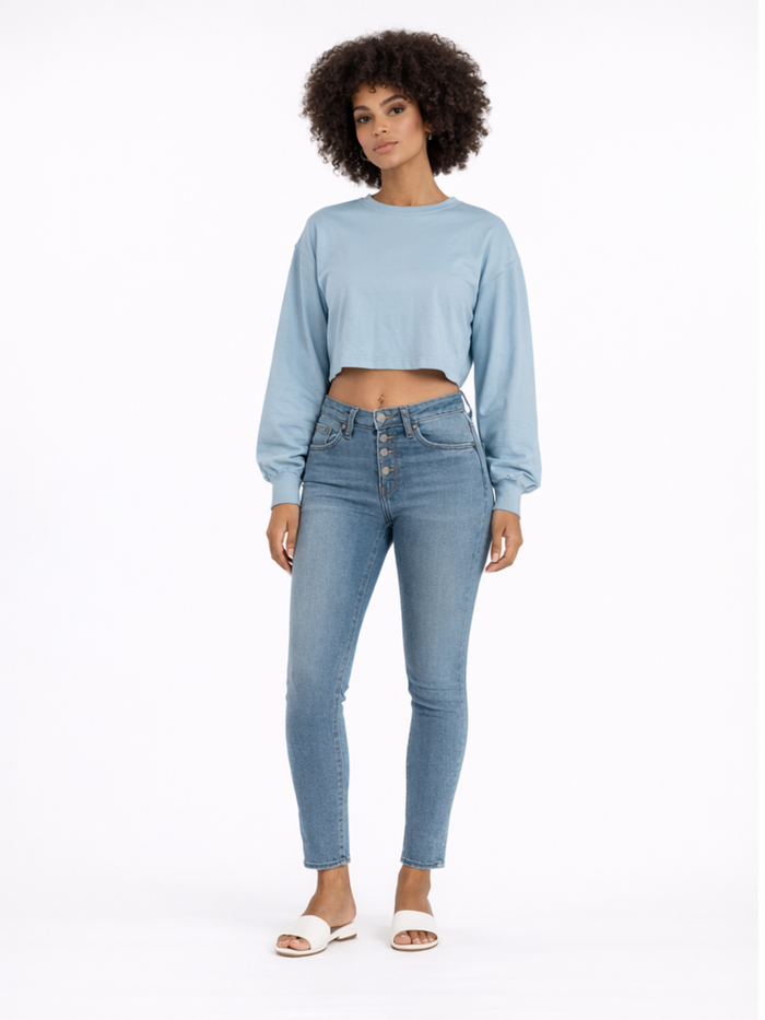 A model wearing a light blue cropped long-sleeve top paired with high-waisted denim jeans and white sandals.